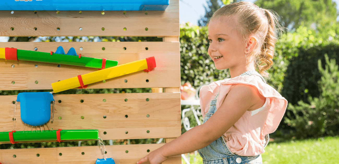 Child playing with a water wall in a garden, developing problem-solving and STEM skills through hands-on outdoor learning with interactive toys.