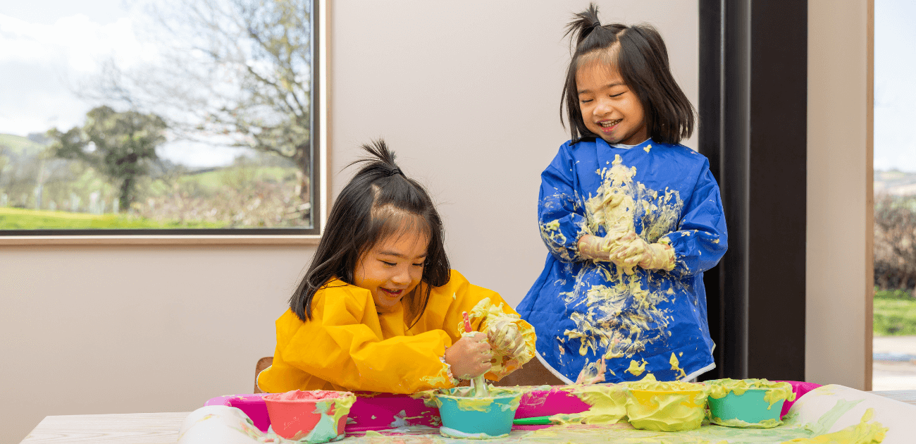 Two kids enjoying sensory play with puffy paint on a play tray, exploring texture and creativity.