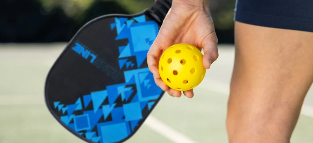a model holding a pickleball racket at ball at their side
