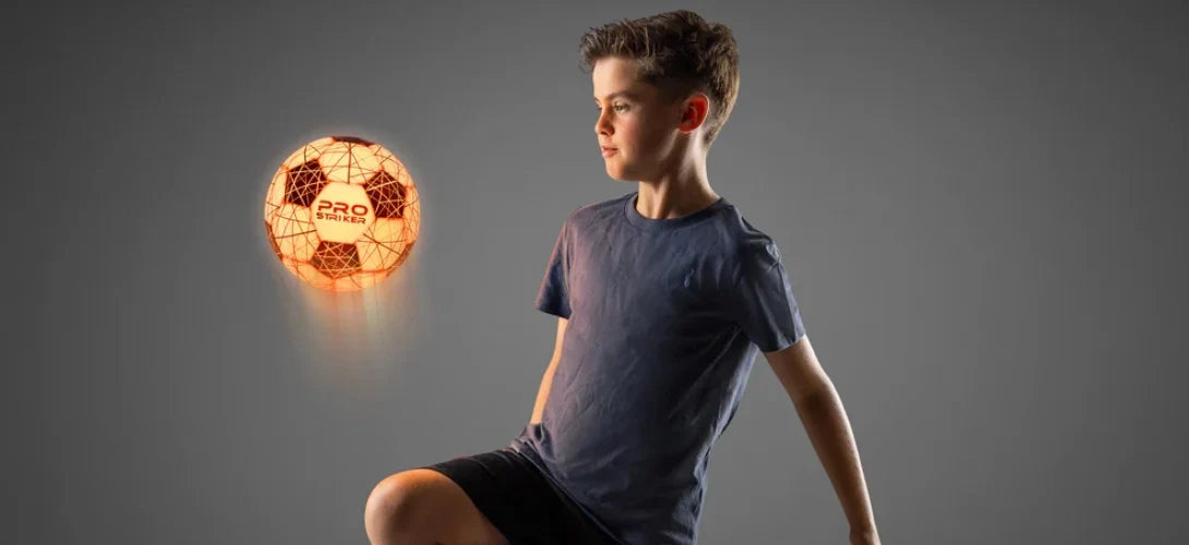 a boy on a black background playing keepy uppies with a glowing orange LED ball
