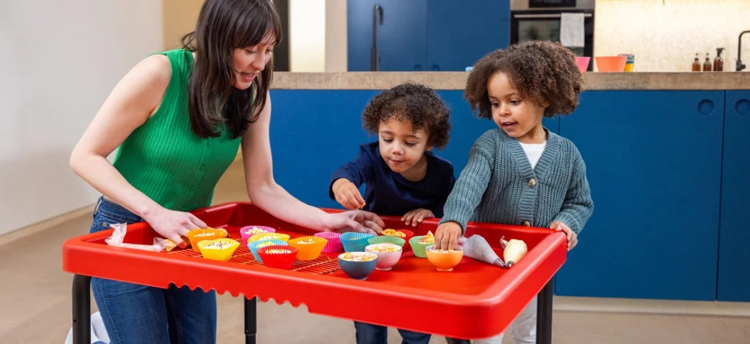 two young children using the Play Tray to decorate cakes with a parent