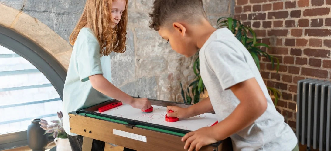 two children playing air hockey on a games table
