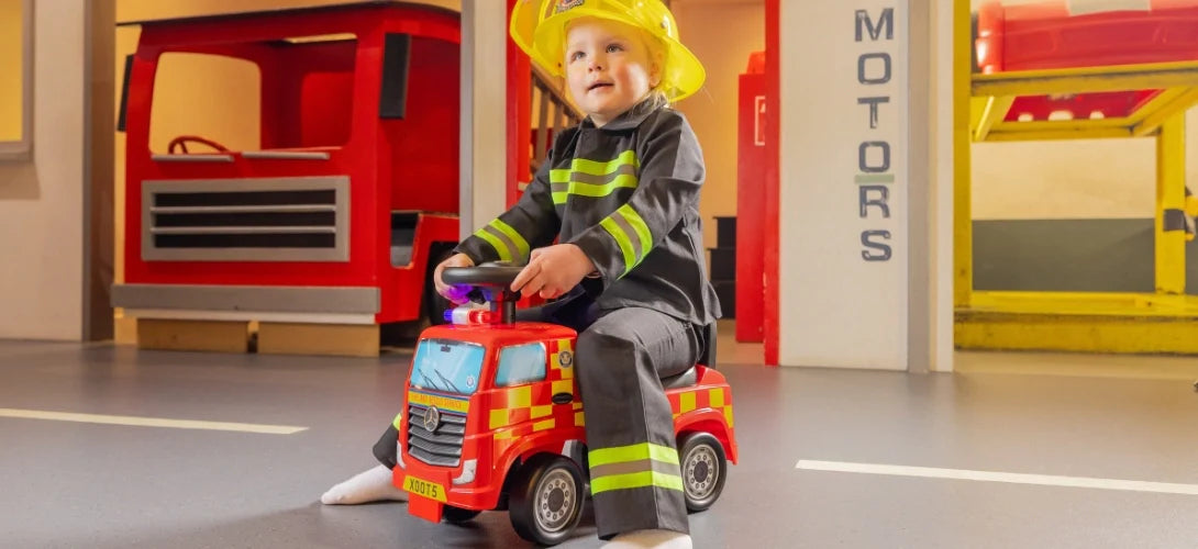 a young child dressed as a fireman riding a foot to floor fire truck ride on
