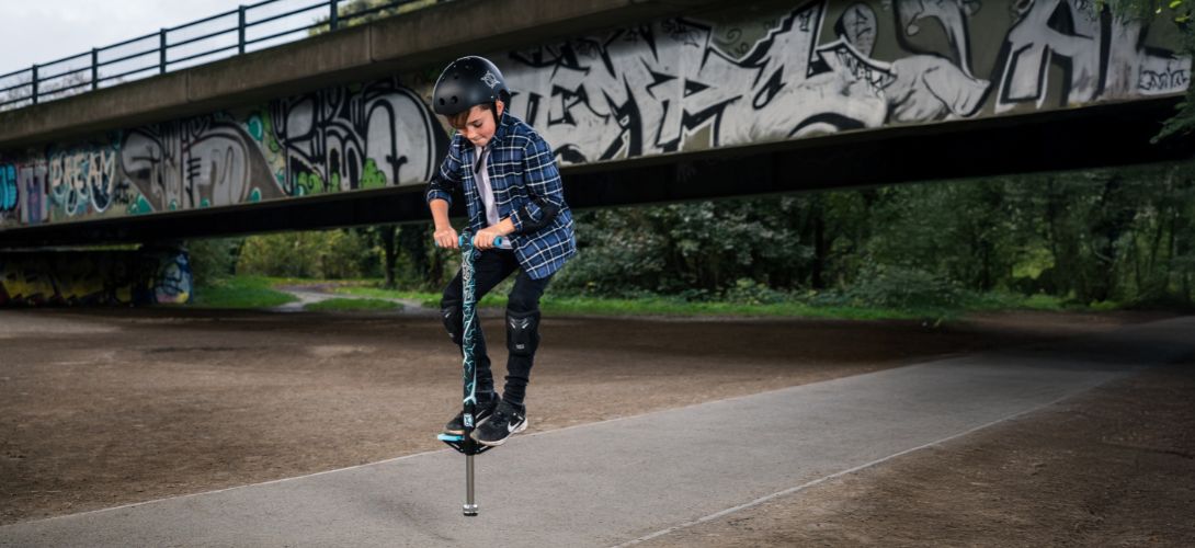A young boy bouncing on a pogo stick against a graffiti backdrop