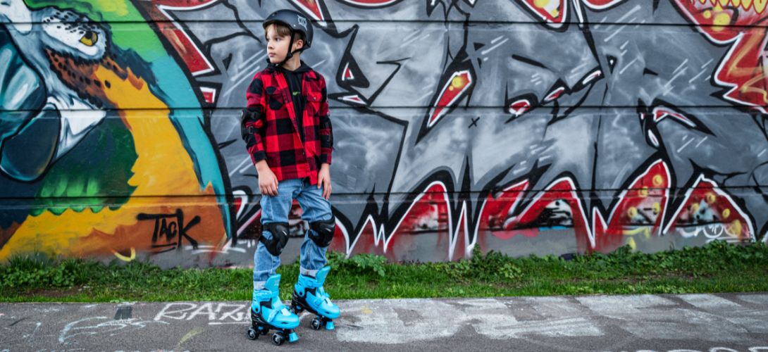 A boy wearing blue and back roller skates against a graffiti wall