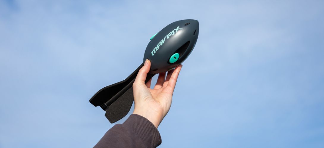 A dark blue and turquise whistle rocket being held in the air with sky in the background