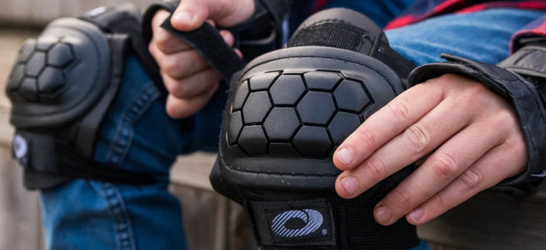 A close up image of a child tightening a pair of black Osprey knee pads