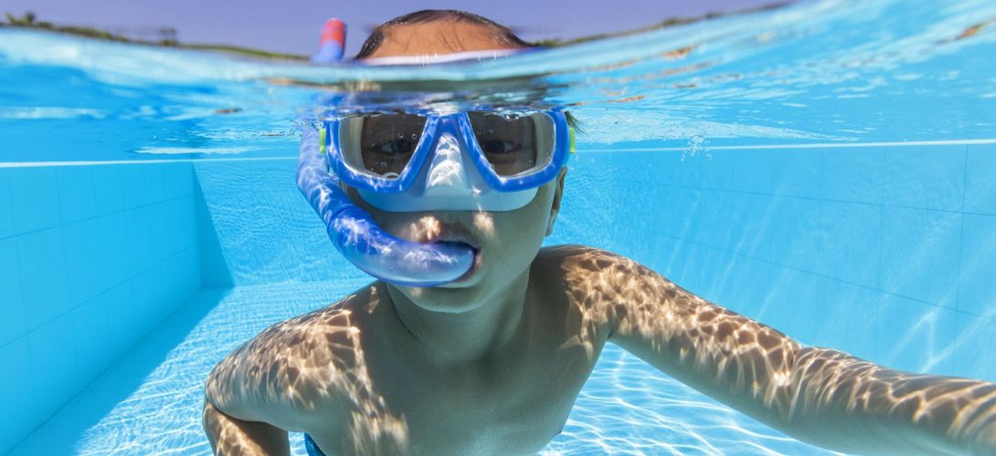 A boy snorkelling underwater towards the camera in a swimming pool