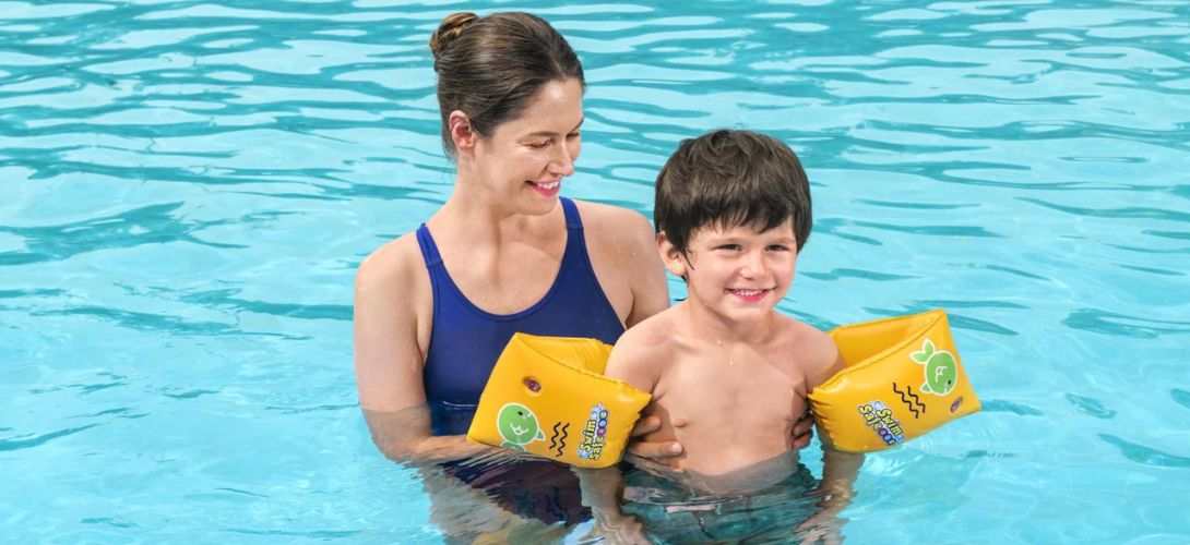 A mum and son in a swimming pool. The son is wearing yellow arm bands