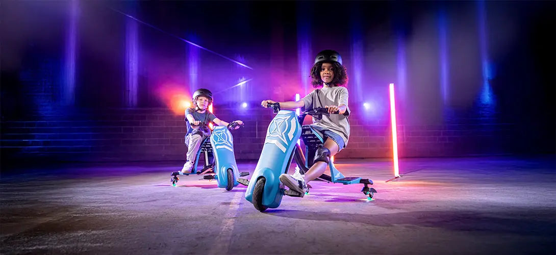A boy sat on a blue and back Cyclone trike inside a warehouse lit with pink and blue lighting